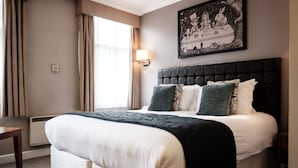 A hotel room with a large bed, a bedside table, a wall-mounted lamp, and a framed picture above the bed. - The Mad Hatter Hotel (London)