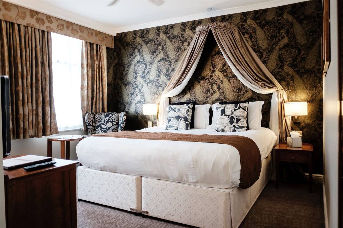 A bedroom with a large bed, a bedside table, a chair, and a desk.
