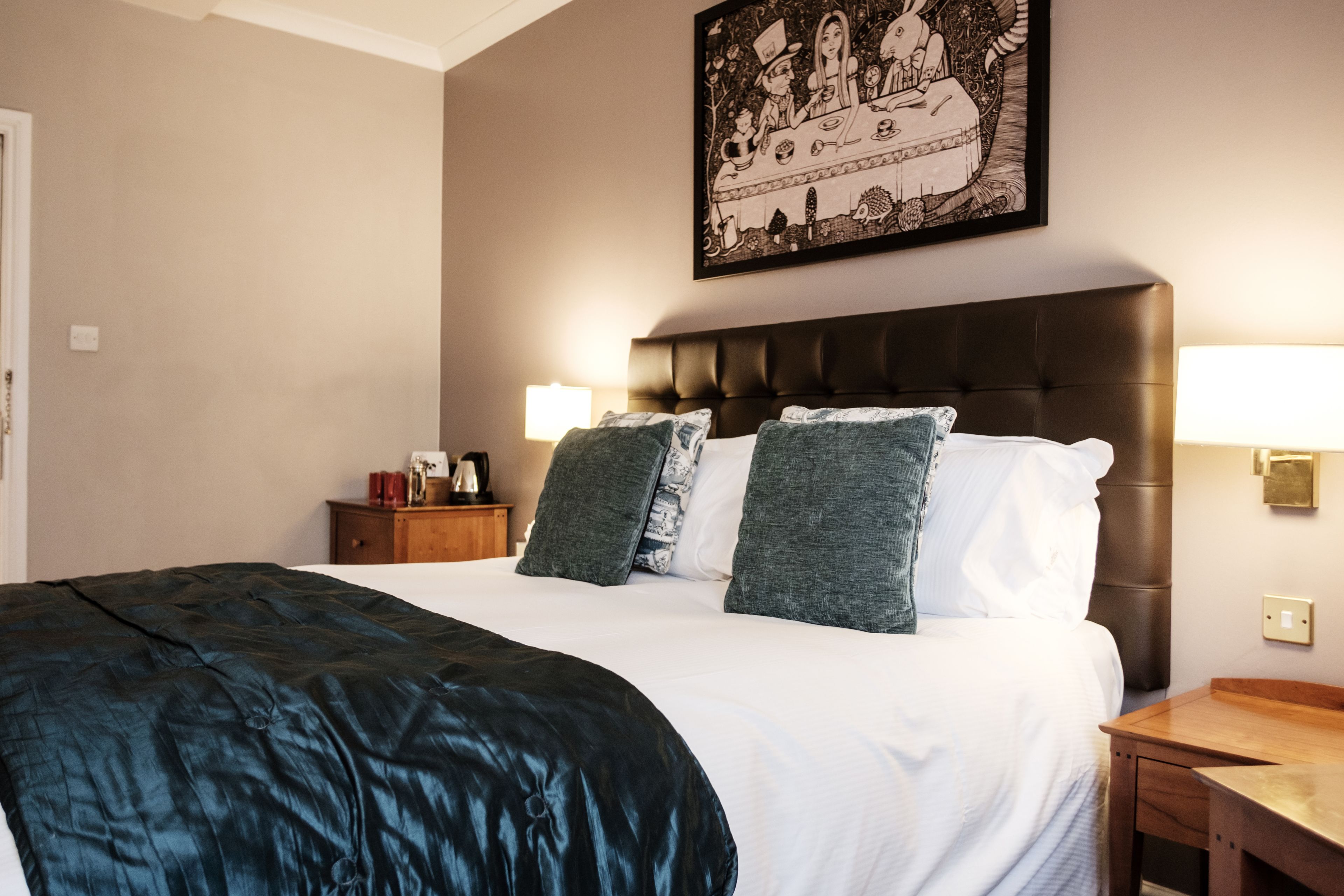 Ett hotellrum med en stor säng, två sänglampor, ett träbord vid sängen och en inramad tavla på väggen.