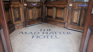 A hotel entrance with a carpet reading "The Mad Hatter Hotel" and signs indicating "Hotel Reception & Toilets" and "Bar and Dining Area". - The Mad Hatter Hotel (London)