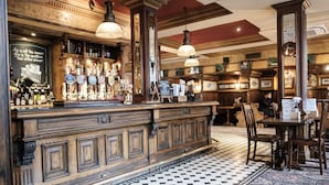 A bar area with a checkered floor, wooden bar counter, and hanging pendant lights. - The Mad Hatter Hotel (London)