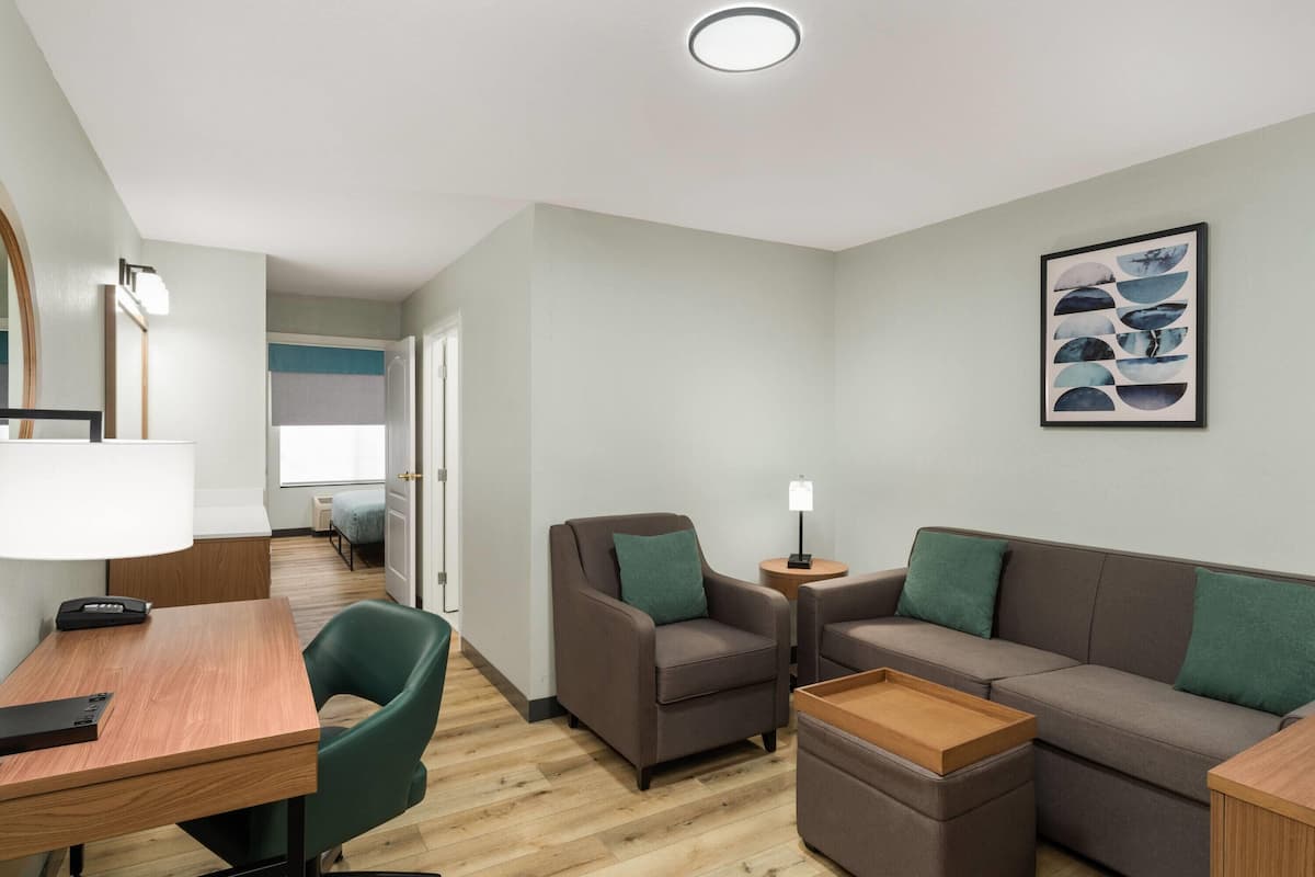 Ein modernes Wohnzimmer mit einem Holztisch, grünem Sessel, braunem Sofa und einem kleinen Beistelltisch mit Lampe.