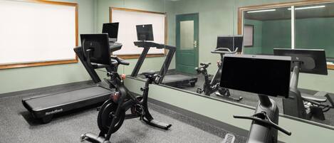 A gym with treadmills, stationary bikes, and a mirrored wall.