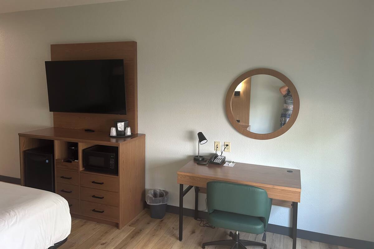 Ein Hotelzimmer mit Bett, Fernseher, Schreibtisch mit Stuhl, Spiegel und Mülleimer.
