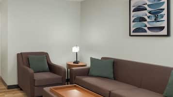 En moderne stue med en brun sofa, en lænestol i brunt, et træsidebord med en lampe, og et abstrakt kunstværk i ramme på væggen.