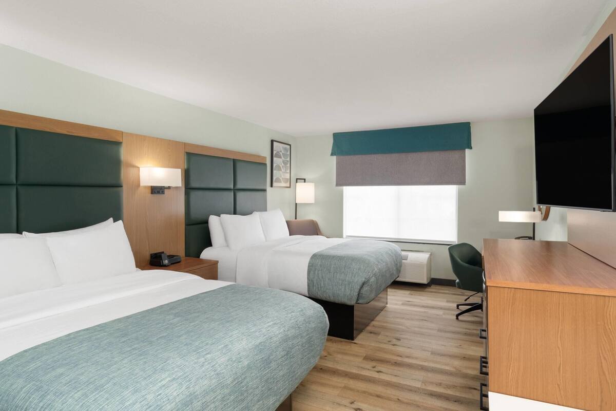 Ein Hotelzimmer mit zwei Betten, einem Schreibtisch, einem Sessel und einem Fernseher.