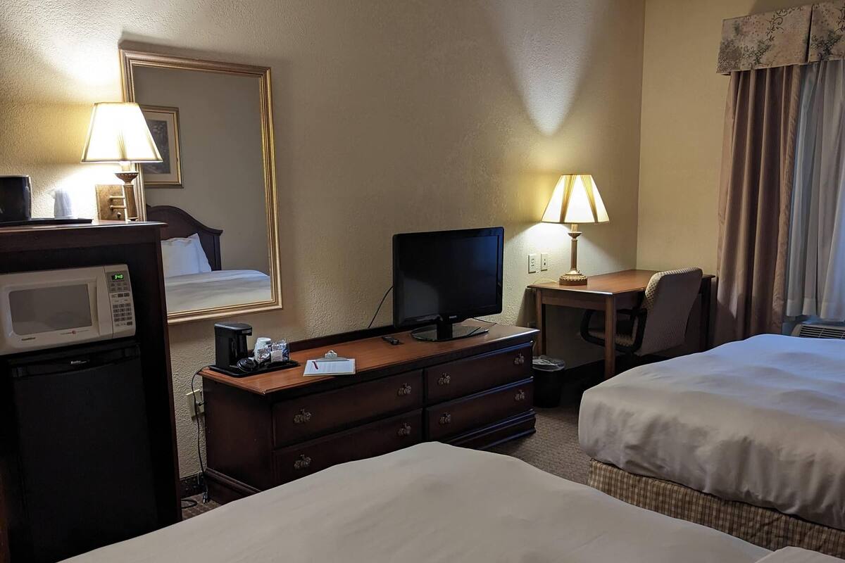 A hotel room with two beds, a desk with a computer, a TV, a microwave, and a dresser.