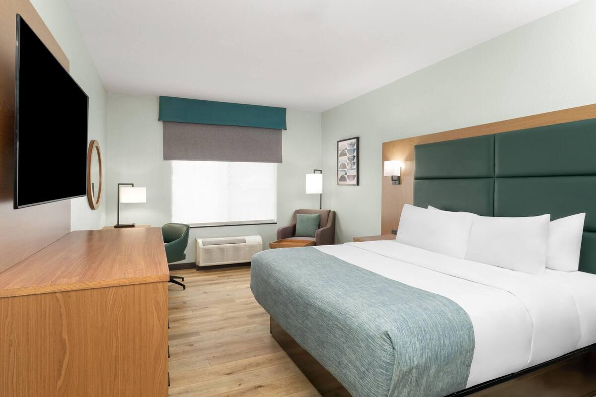 Ein Hotelzimmer mit einem großen Bett, einem Schreibtisch, einem Sessel, einem Fernseher und einem Fenster mit Aussicht.