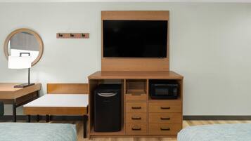 Quarto de hotel com cama, escrivaninha, espelho, televisão, micro-ondas e mini-geladeira.