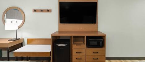 Een hotelkamer met een bed, een bureau, een spiegel, een televisie, een magnetron en een minibar.