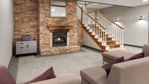 A living room with a stone fireplace, a staircase, and a sofa. - Wingate Suites By Wyndham Mansfield (Mansfield)