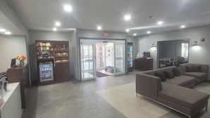 A spacious lobby with a reception desk, vending machines, a seating area with sofas, and a glass door entrance. - Wingate Suites By Wyndham Mansfield (Mansfield)
