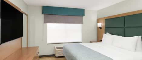 A hotel room with a bed, a flat-screen TV, a wooden desk, and a window with blinds.