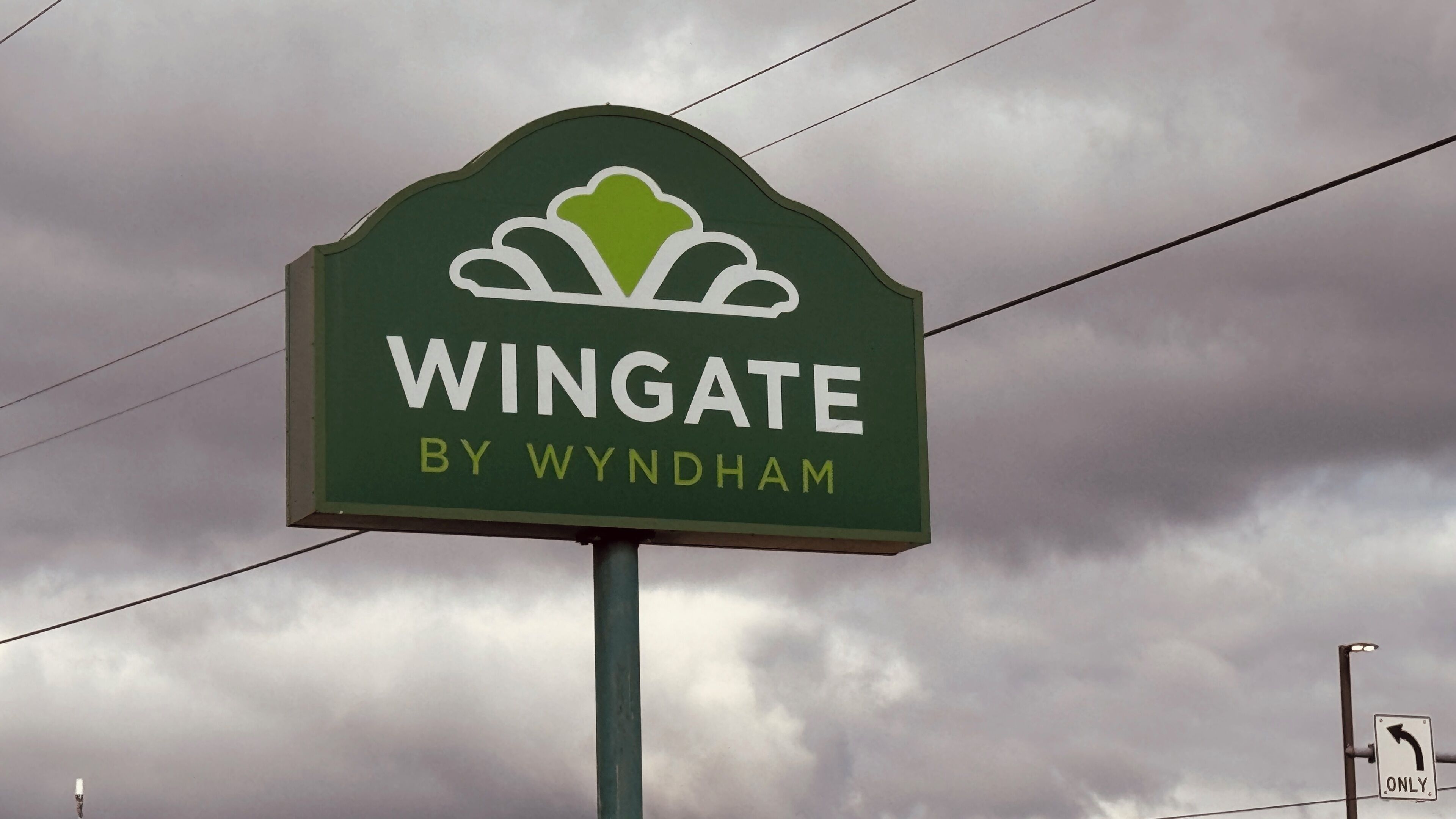 A sign with the text "Wingate by Wyndham" against a cloudy sky.
