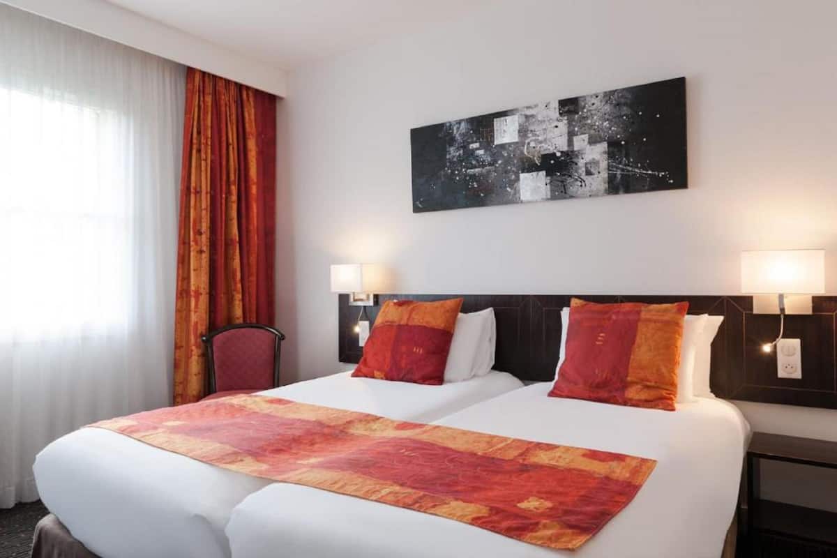 Ein Hotelzimmer mit einem großen Bett, zwei Nachttischlampen, einem Kopfteil und einem Stadtbild an der Wand.