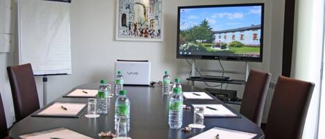 Un salón de conferencias con una mesa redonda, sillas, una pizarra, una pantalla de proyector y un cuadro en la pared.