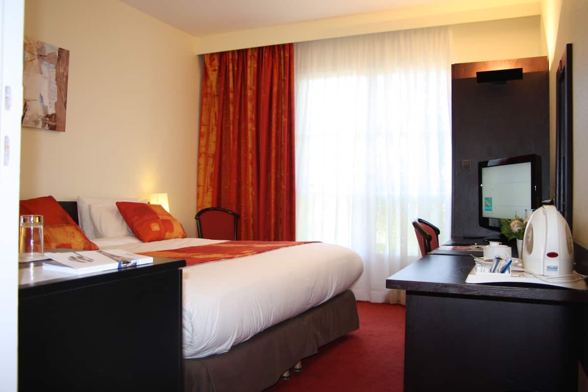 A hotel room with a bed, desk, chair, TV, and a window with curtains.