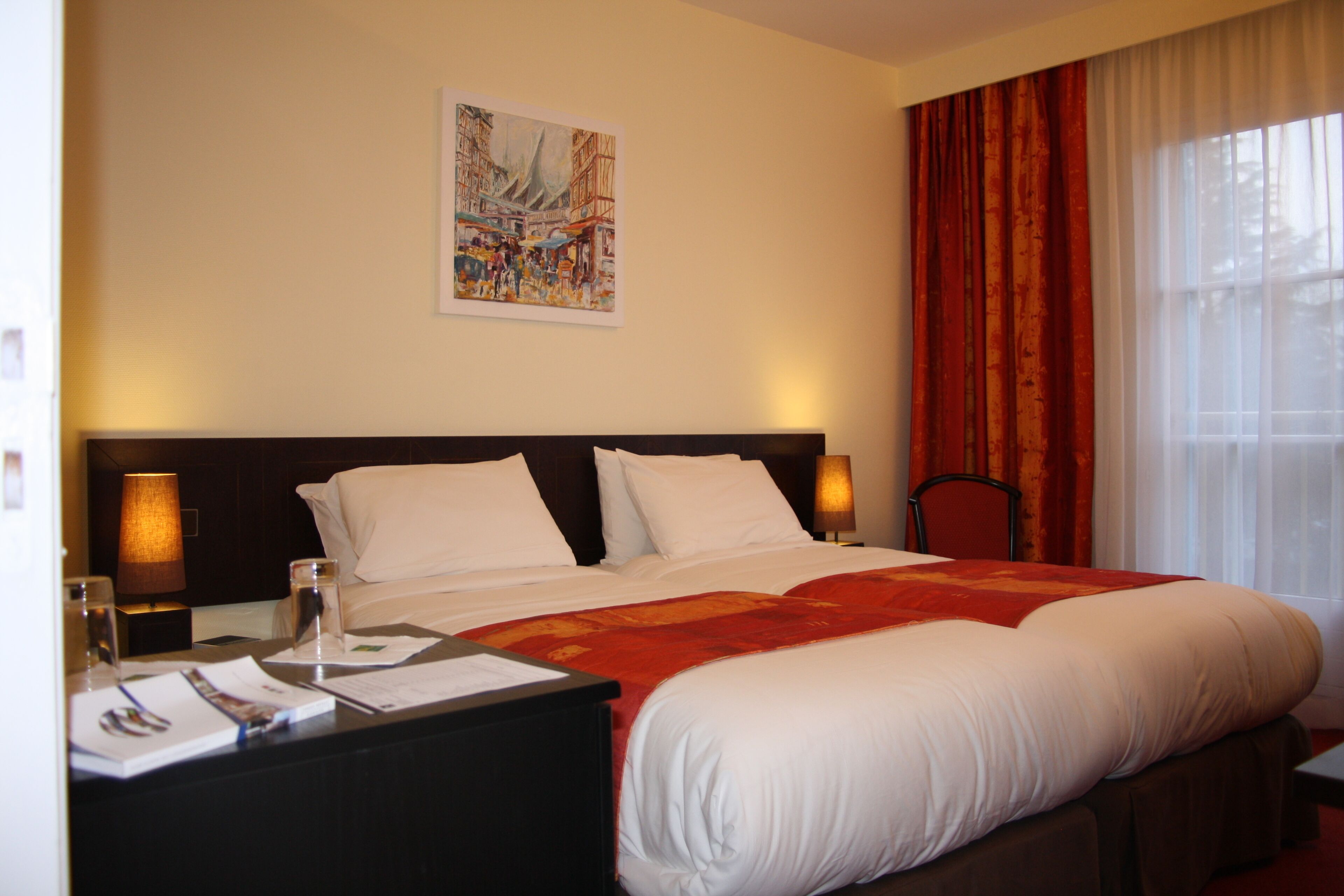 Ein Hotelzimmer mit einem großen Bett, einem Nachttisch mit Lampe, einem Gemälde an der Wand und einem Fenster mit Vorhängen.