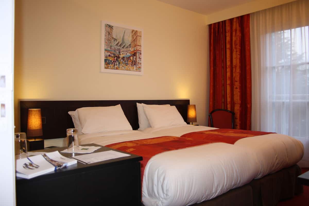 A hotel room with a large bed, a nightstand with a lamp, a painting on the wall, and a window with curtains.