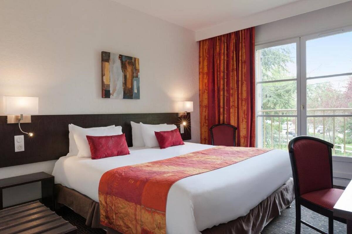 Ein Hotelzimmer mit einem großen Bett, zwei Nachttischlampen, einem mit Vorhängen versehenen Fenster und einem Bild an der Wand.