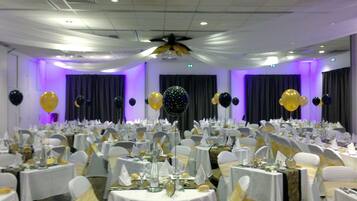 Une salle de banquet avec des tables rondes dressées pour un événement formel, agrémentée de nappes blanches et de rubans dorés sur les chaises.