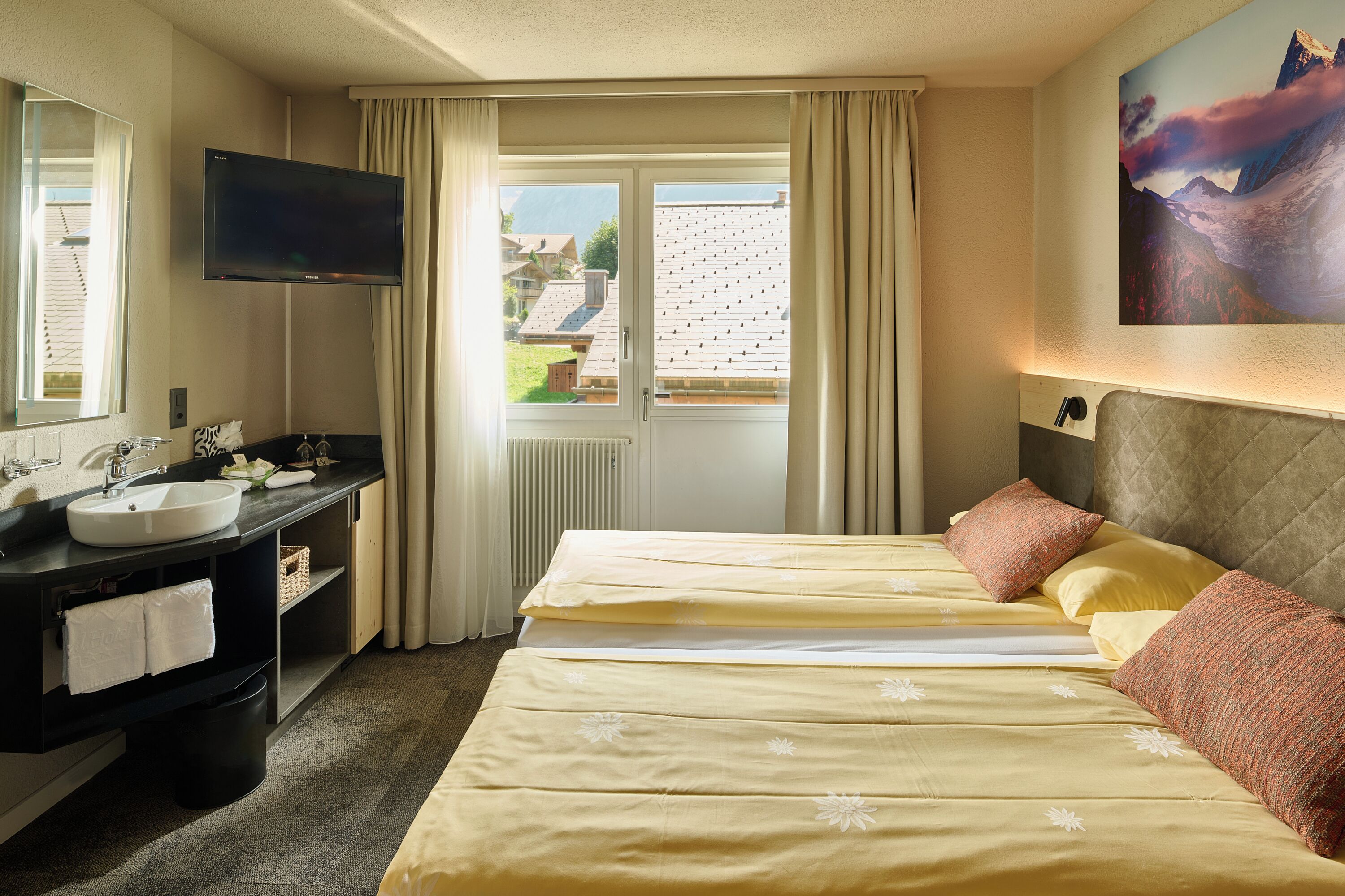 Una habitación de hotel con cama, televisor, baño con lavamanos y ventana con cortinas.