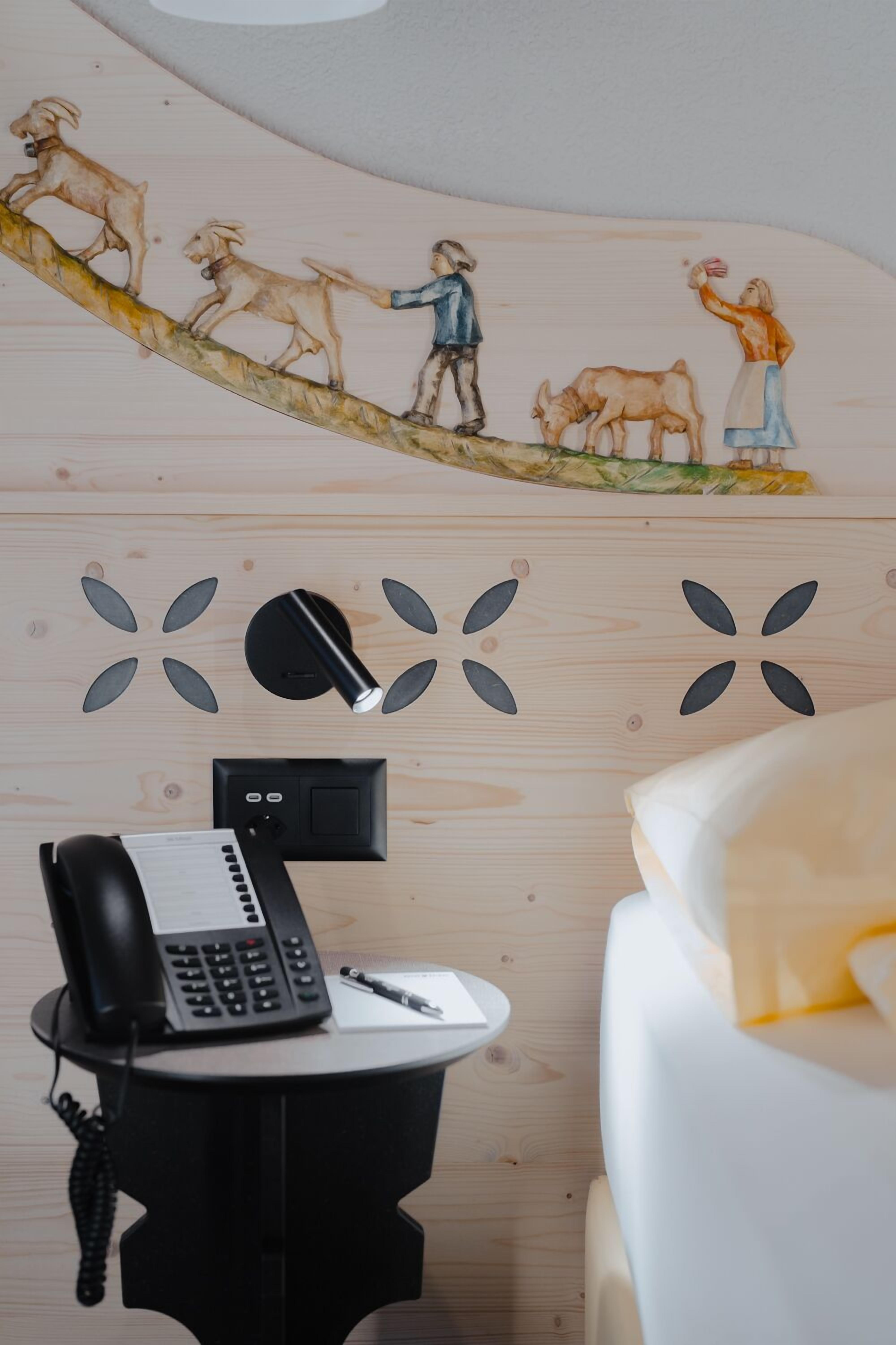 A room with a wooden wall, a bed, a desk with a phone, and a wall decoration.