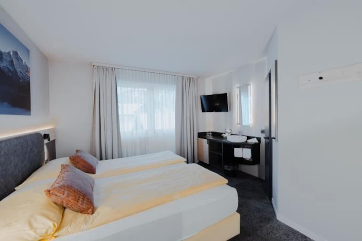 A hotel room with two beds, a desk with a mirror, a TV, and a painting on the wall.