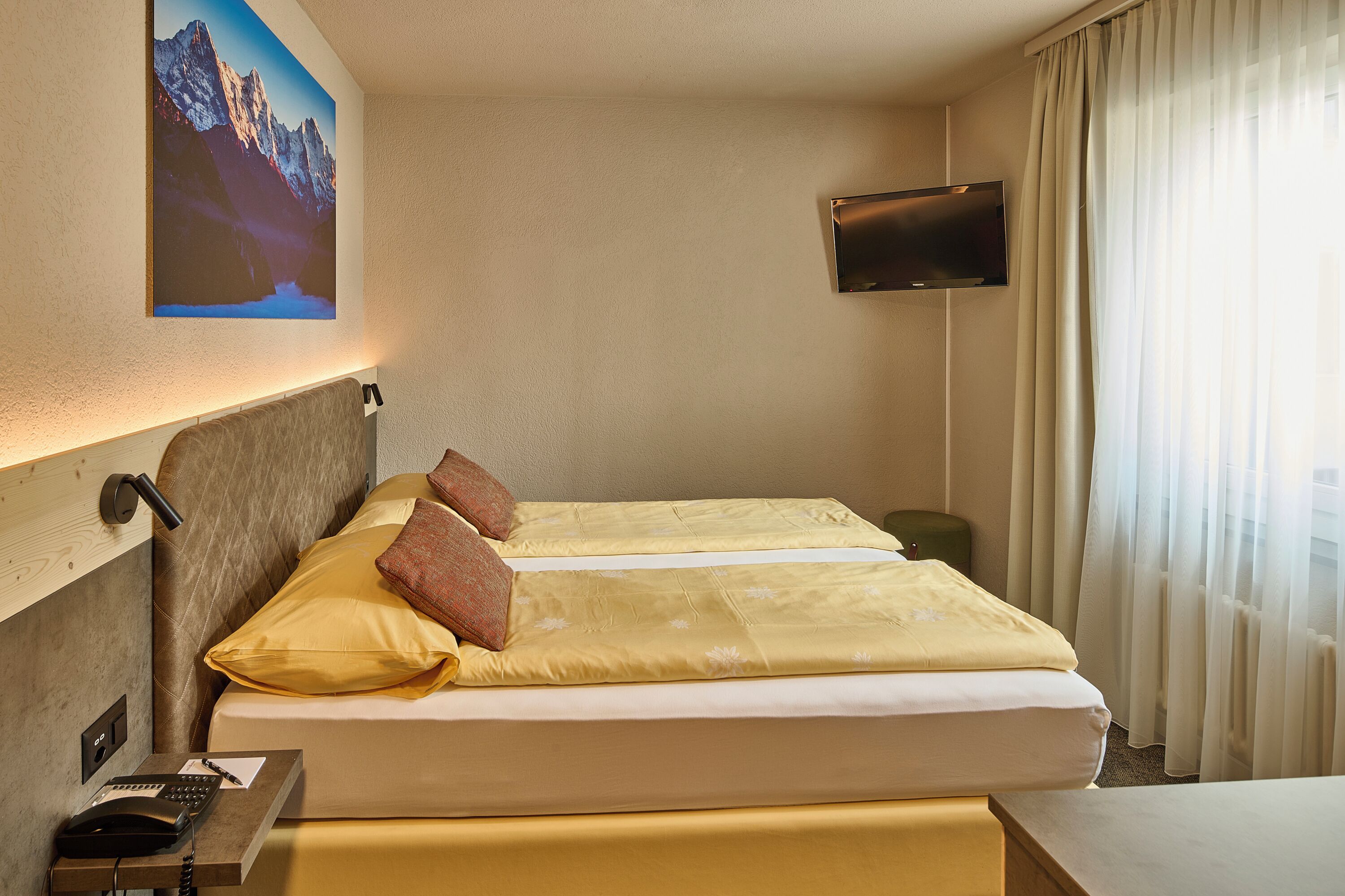 Hotelkamer met een bed, een bureau met telefoon, een flatscreen-televisie aan de muur en een berglandschap op de muur.
