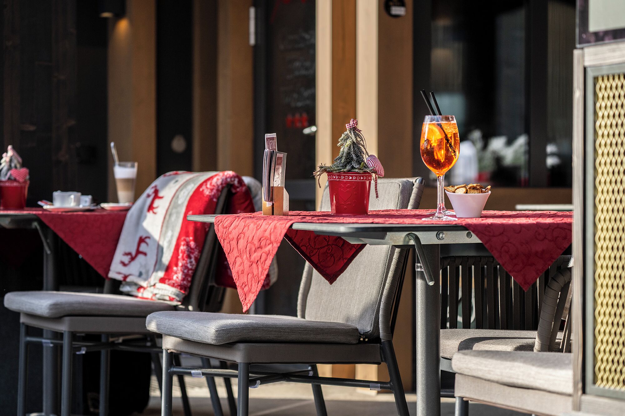 Des tables installées en plein air, recouvertes de nappes rouges, un petit sapin de Noël et un verre de boisson à l’orange.