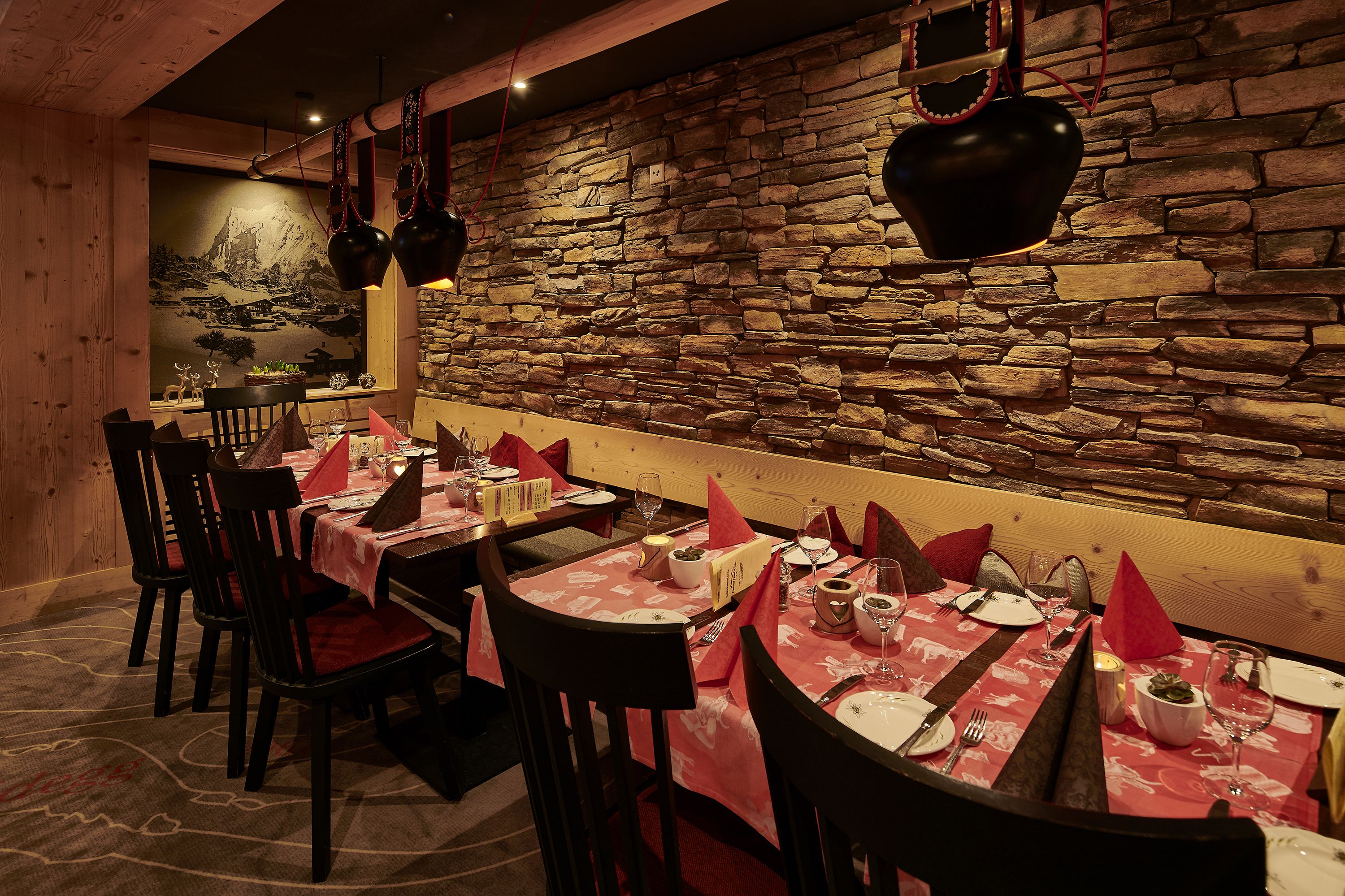 A restaurant with stone walls, wooden furniture, and red tablecloths.