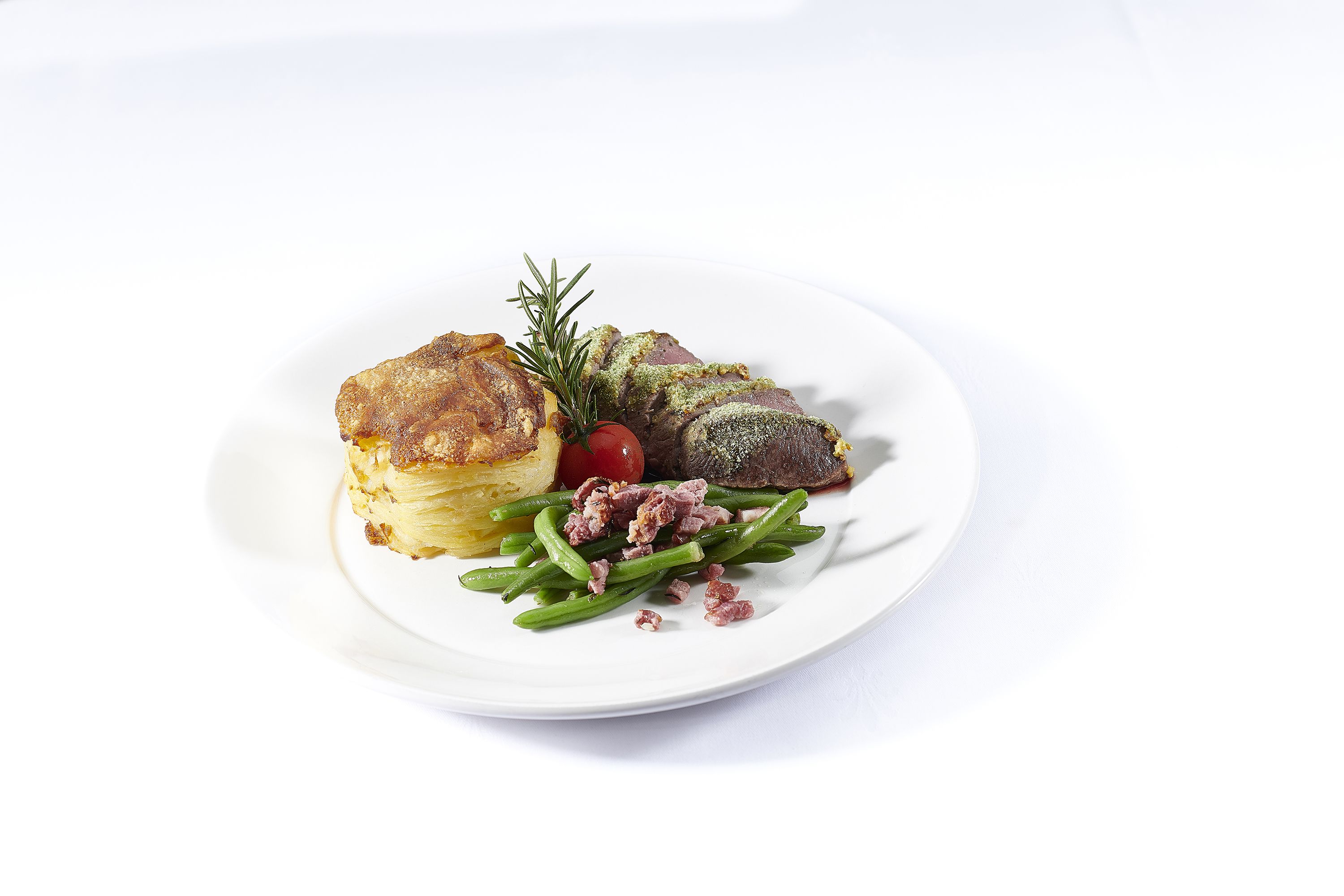 A plate with a pastry, green beans, a small tomato, and a sprig of rosemary.