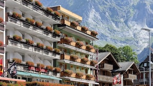 Un hotel con varios balcones decorados con flores, un telón de fondo montañoso y un estilo arquitectónico suizo tradicional.