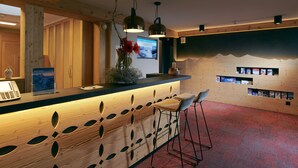 Un área de recepción con un mostrador de madera, taburetes, una computadora y un televisor montado en la pared.