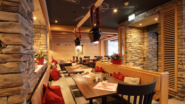 Un restaurante con paredes de piedra, mesas de madera y cojines rojos.