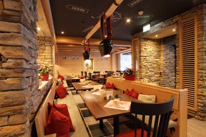A restaurant with stone walls, wooden tables, and red cushions. - Central Hotel Wolter (Grindelwald)