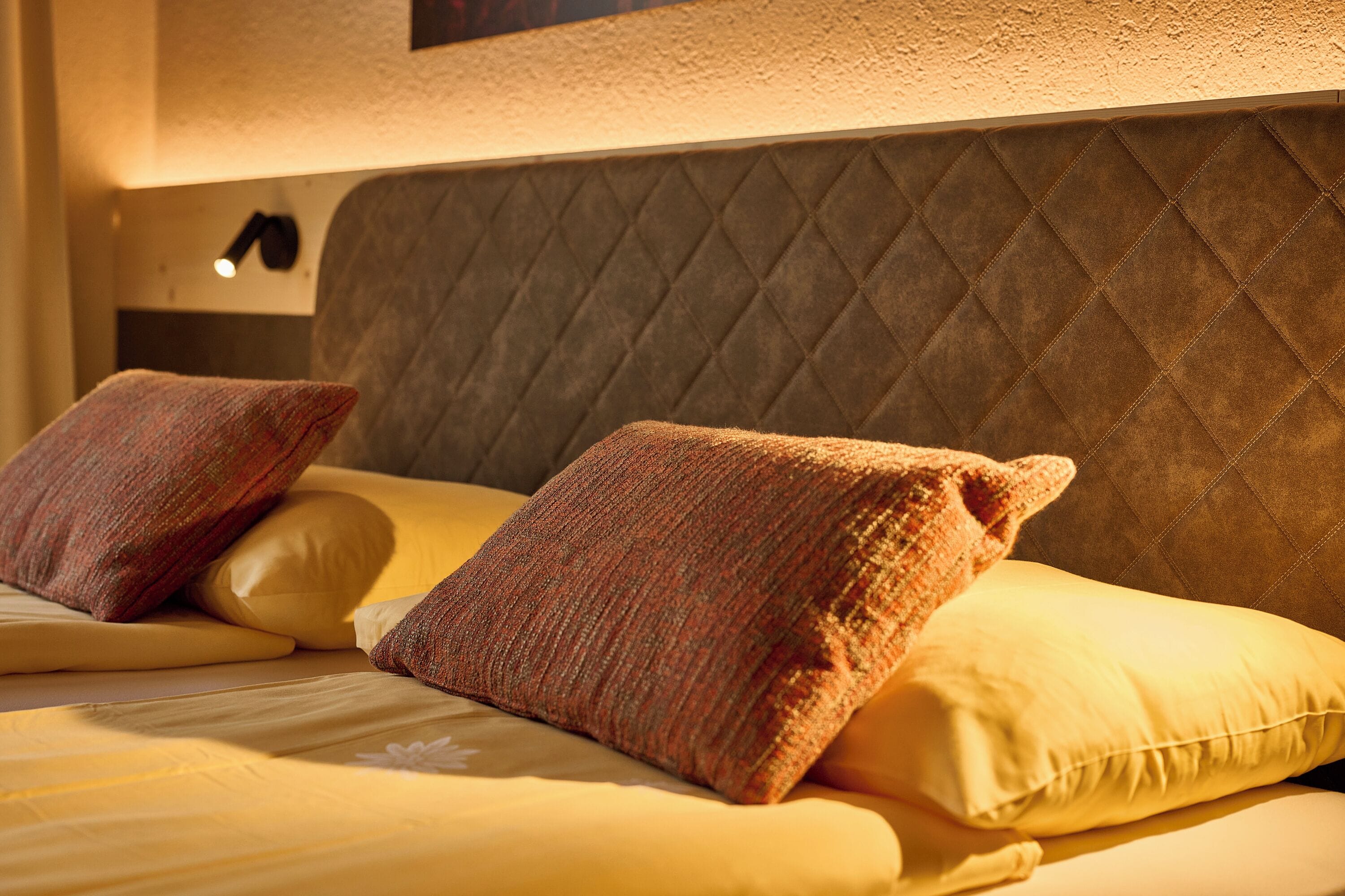Una cama con cabecera acolchada, dos almohadas y una lámpara de noche.