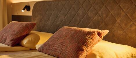Una cama con cabecera acolchada, dos almohadas y una lámpara de noche.