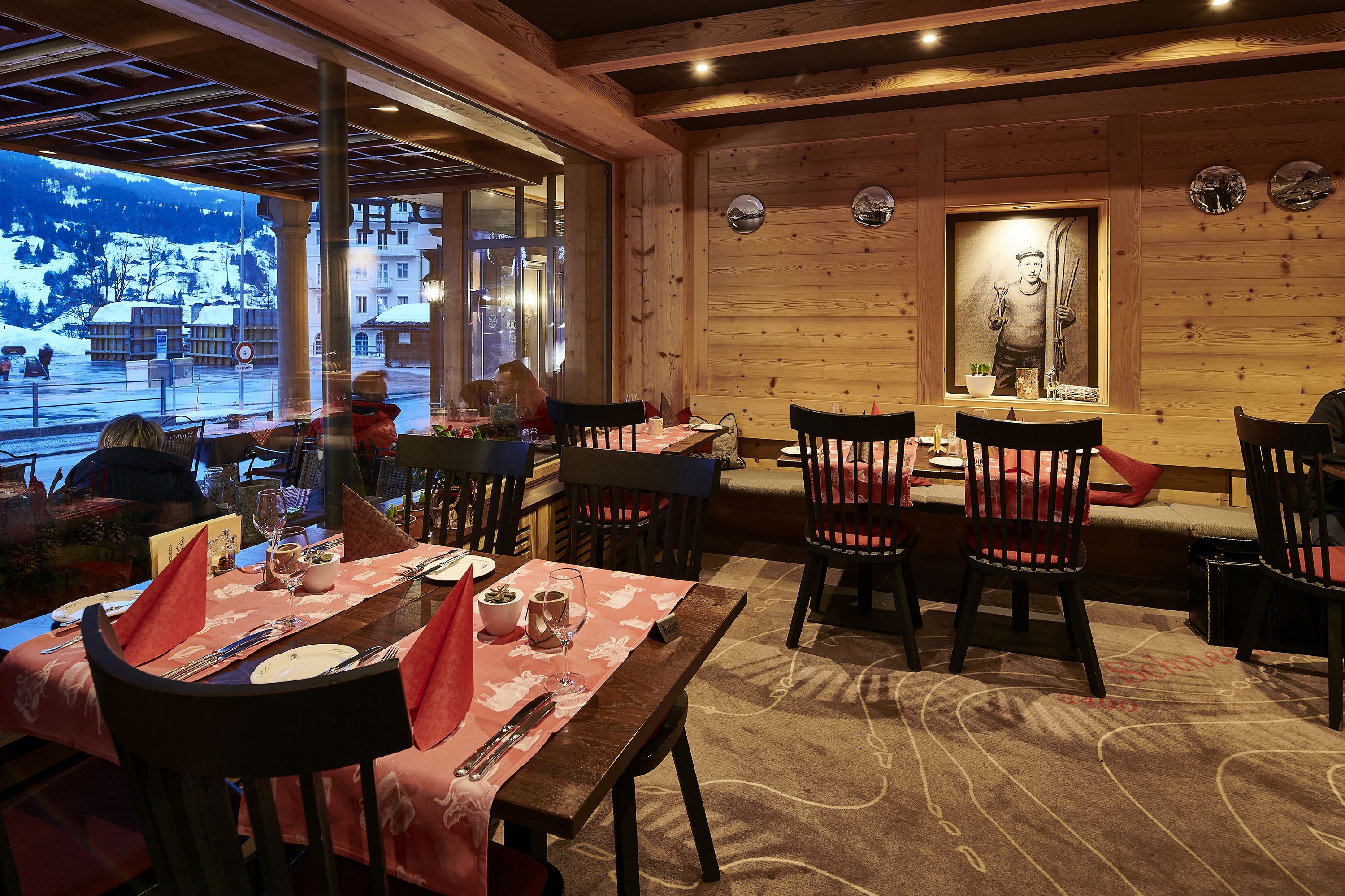 Un restaurante con paredes de madera, un cuadro con temática de esquí y vistas a una montaña nevada.