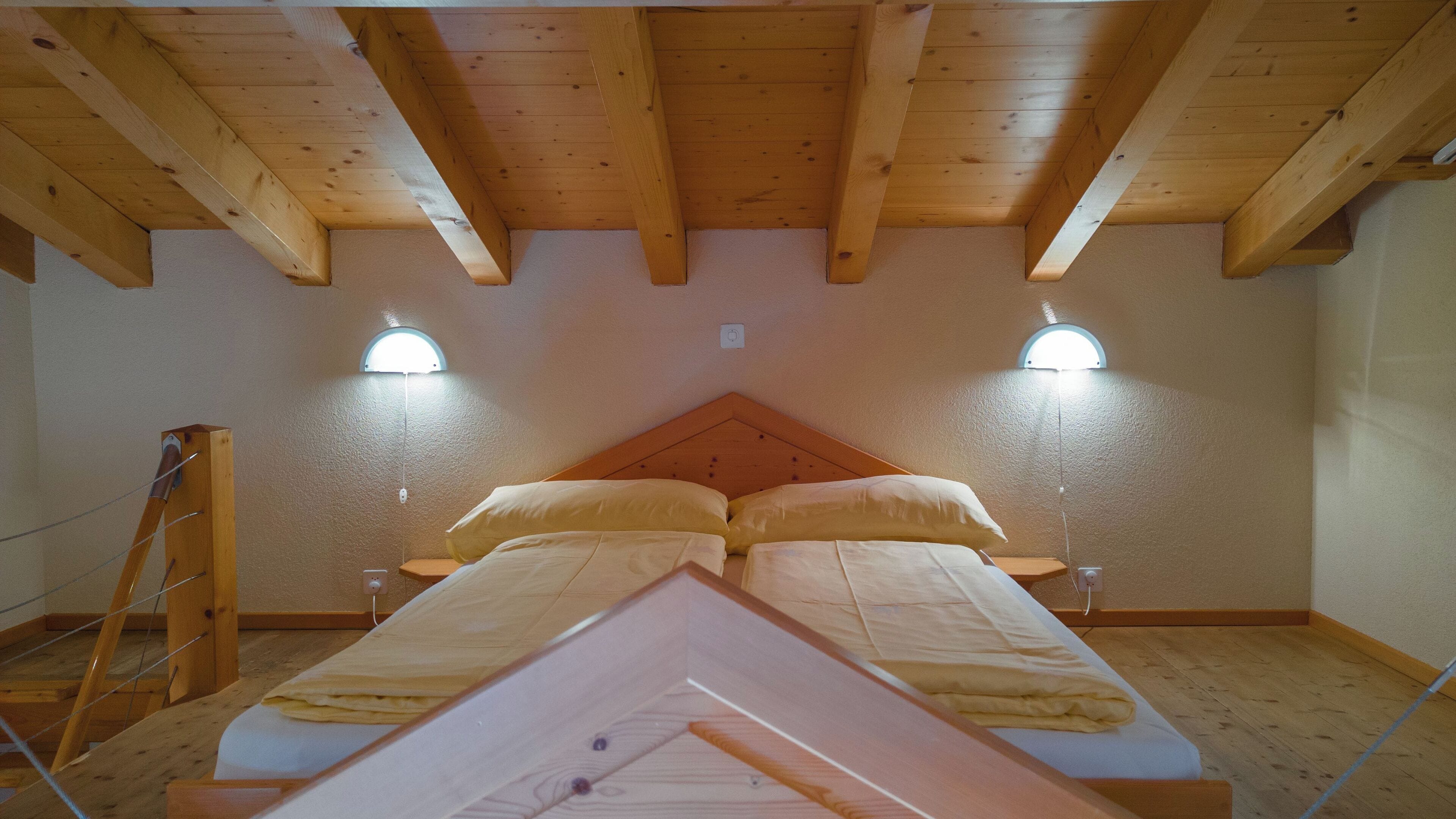 Ein Zimmer mit Holzboden, zwei Nachttischlampen, einem Bett mit zwei Kissen und einer Holzleiter.