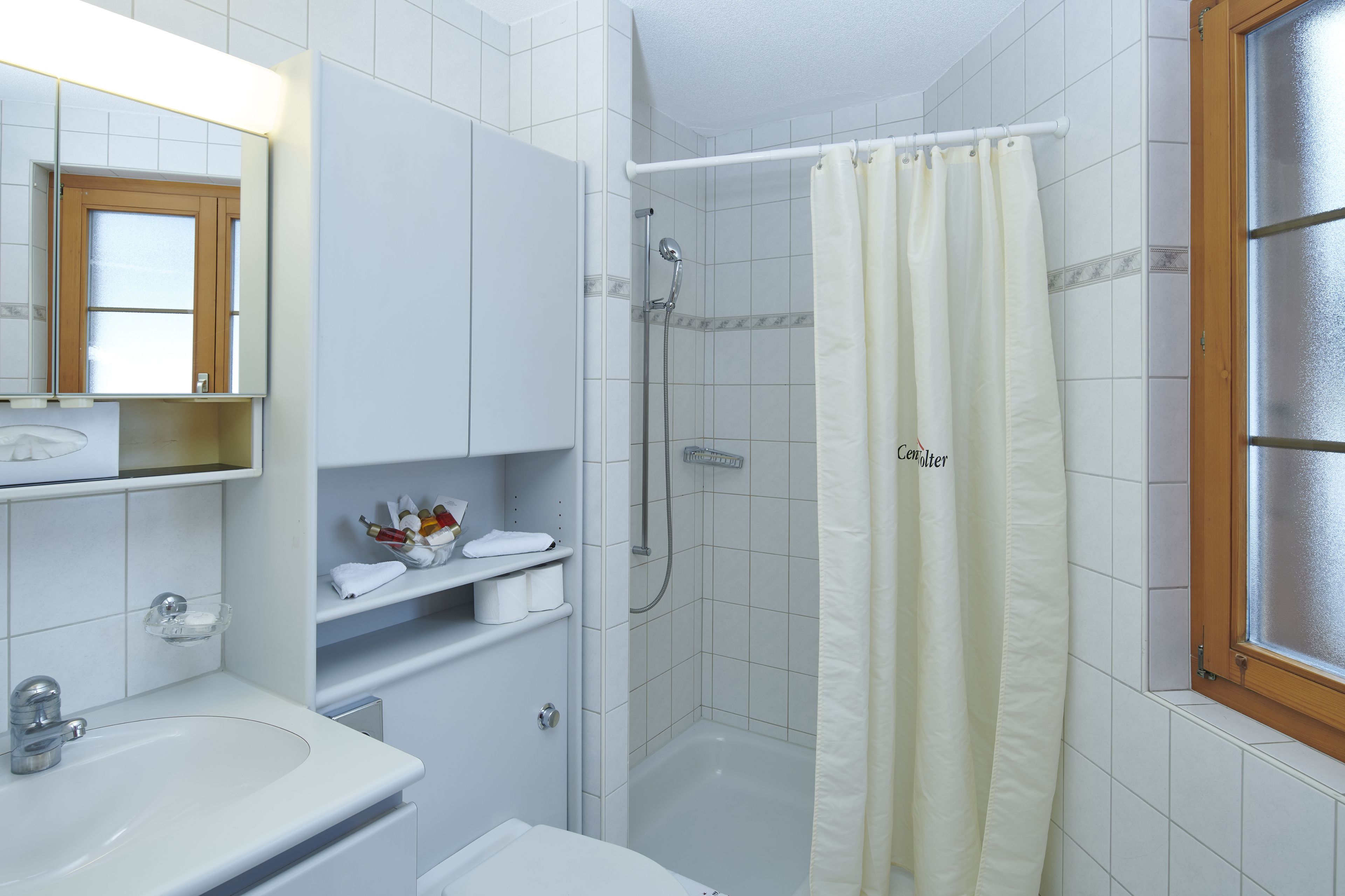 Un baño con lavamanos blanco, espejo y zona de ducha.
