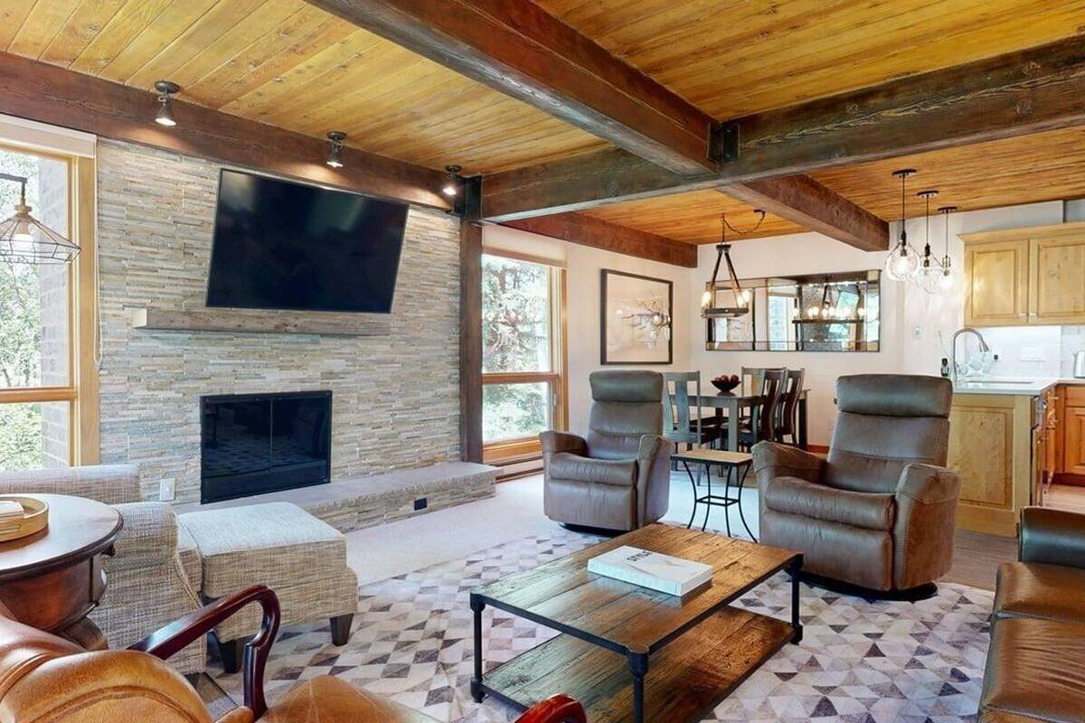 A spacious living room with a stone fireplace, leather sofas, and a large TV mounted on the wall.