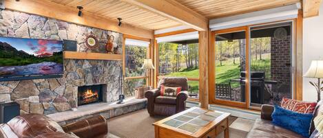 Una sala de estar acogedora con chimenea de piedra, sofás de cuero y un amplio ventanal con vistas al exterior.