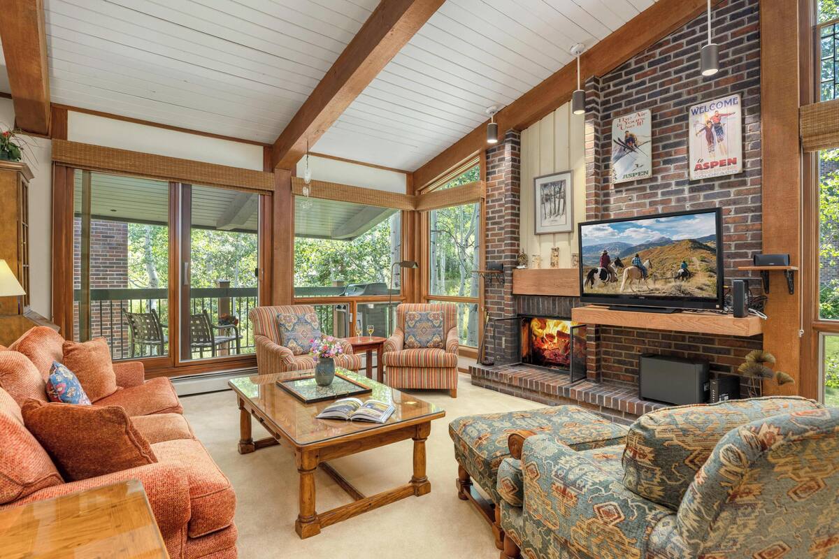 A spacious living room with a fireplace, comfortable seating, and large windows offering a view of the outdoors.