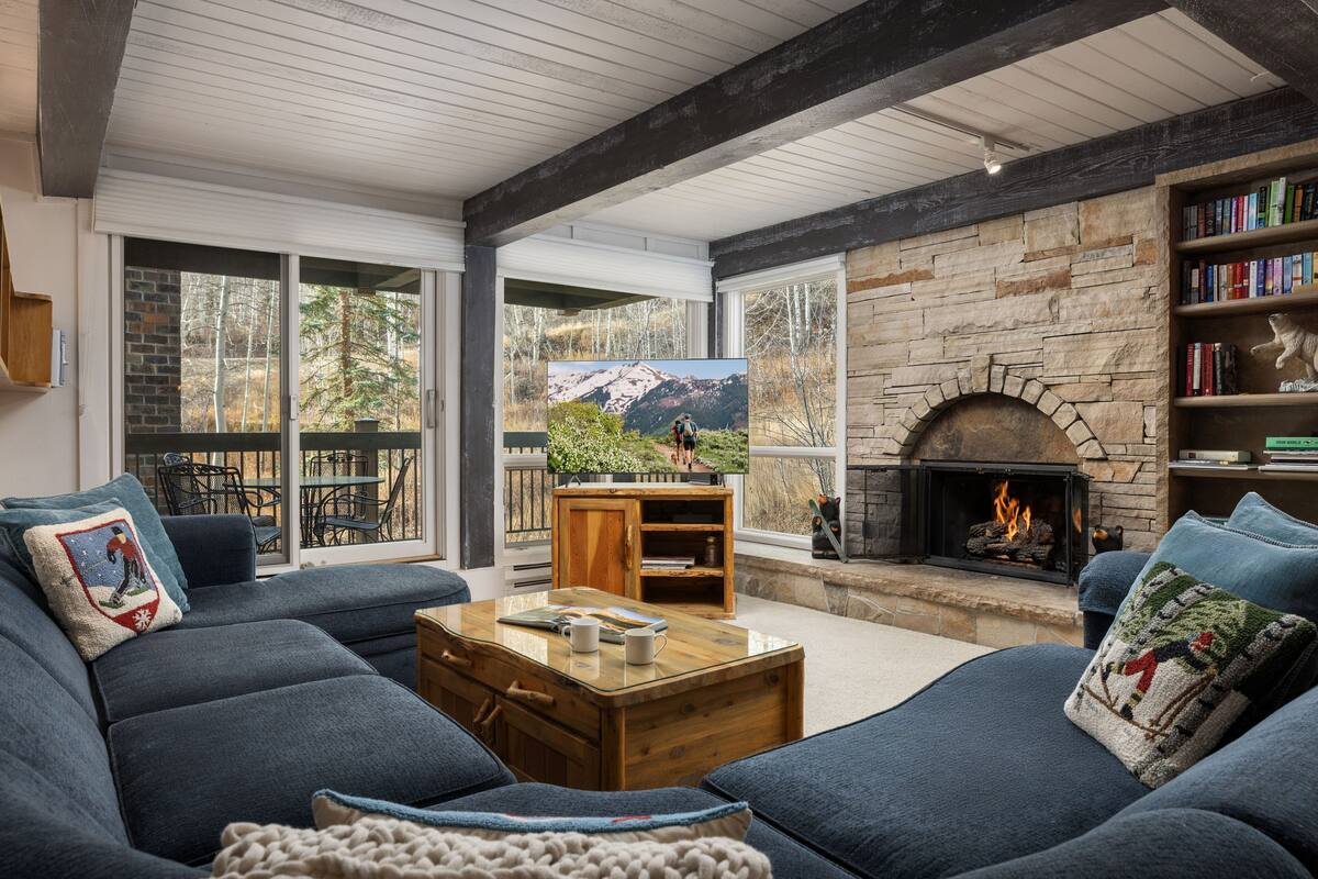 A cozy living room with a fireplace, large windows, and a comfortable seating area.