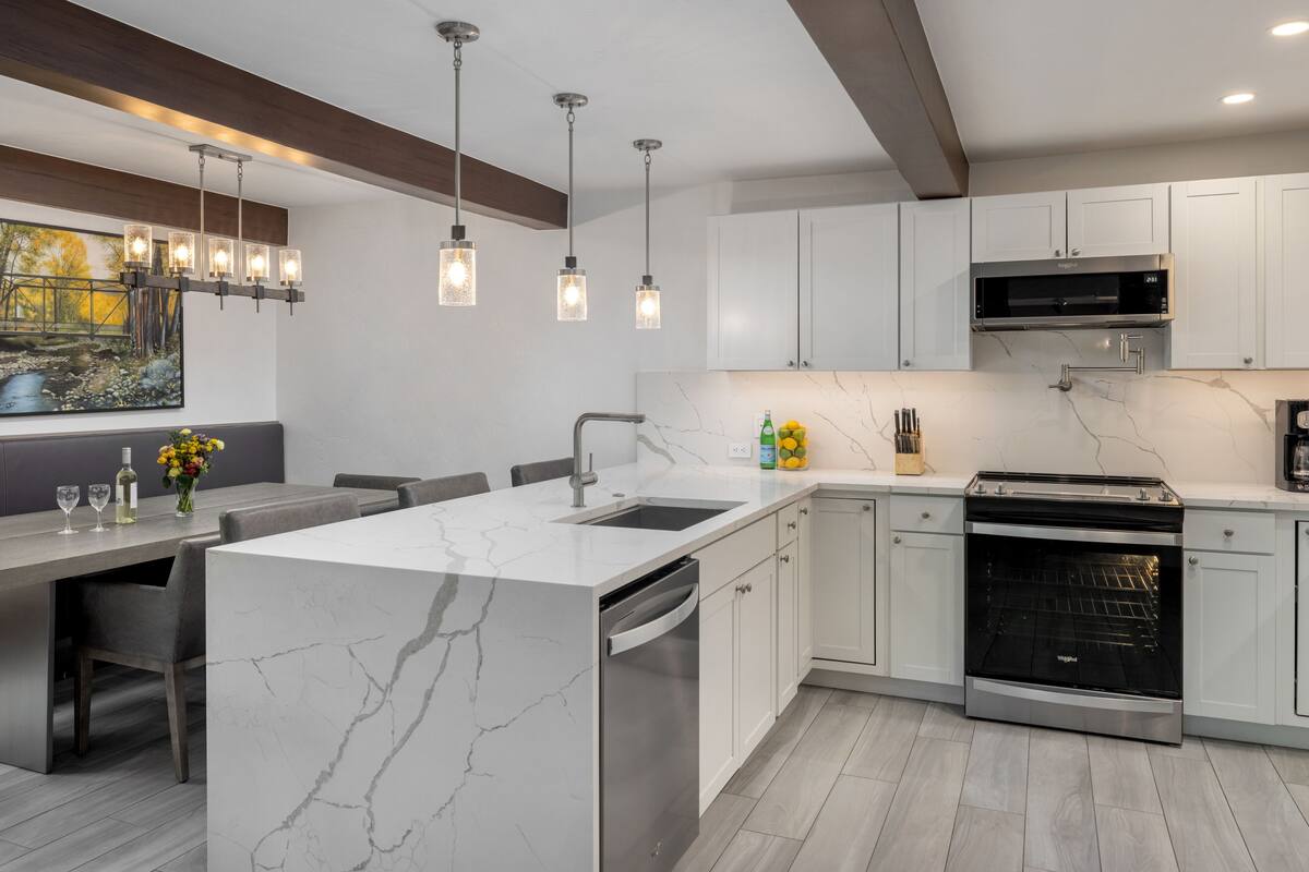 A modern kitchen with white cabinets, a marble island, and pendant lighting.