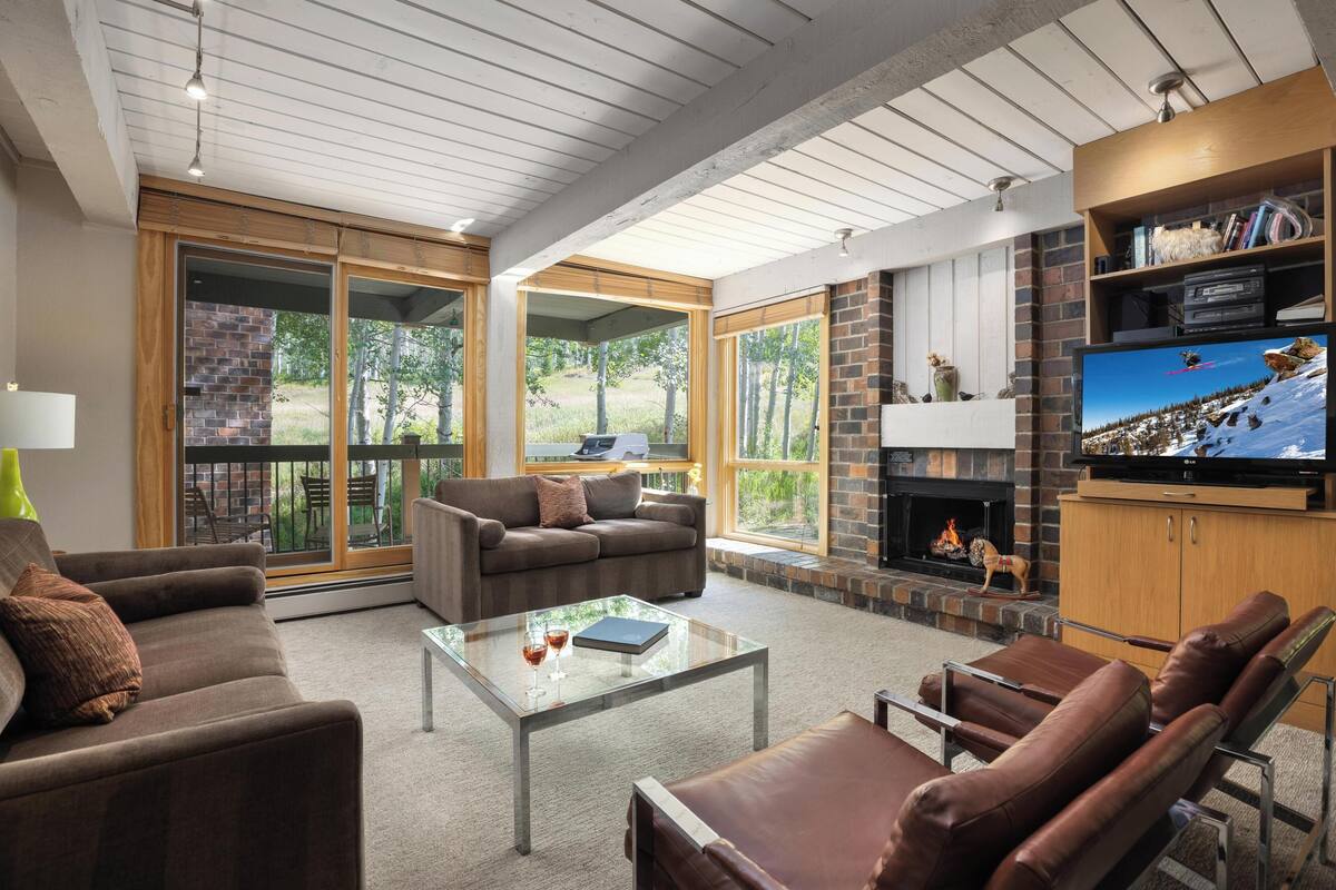 A spacious living area with a fireplace, comfortable seating, and large windows offering a view of the outdoors.