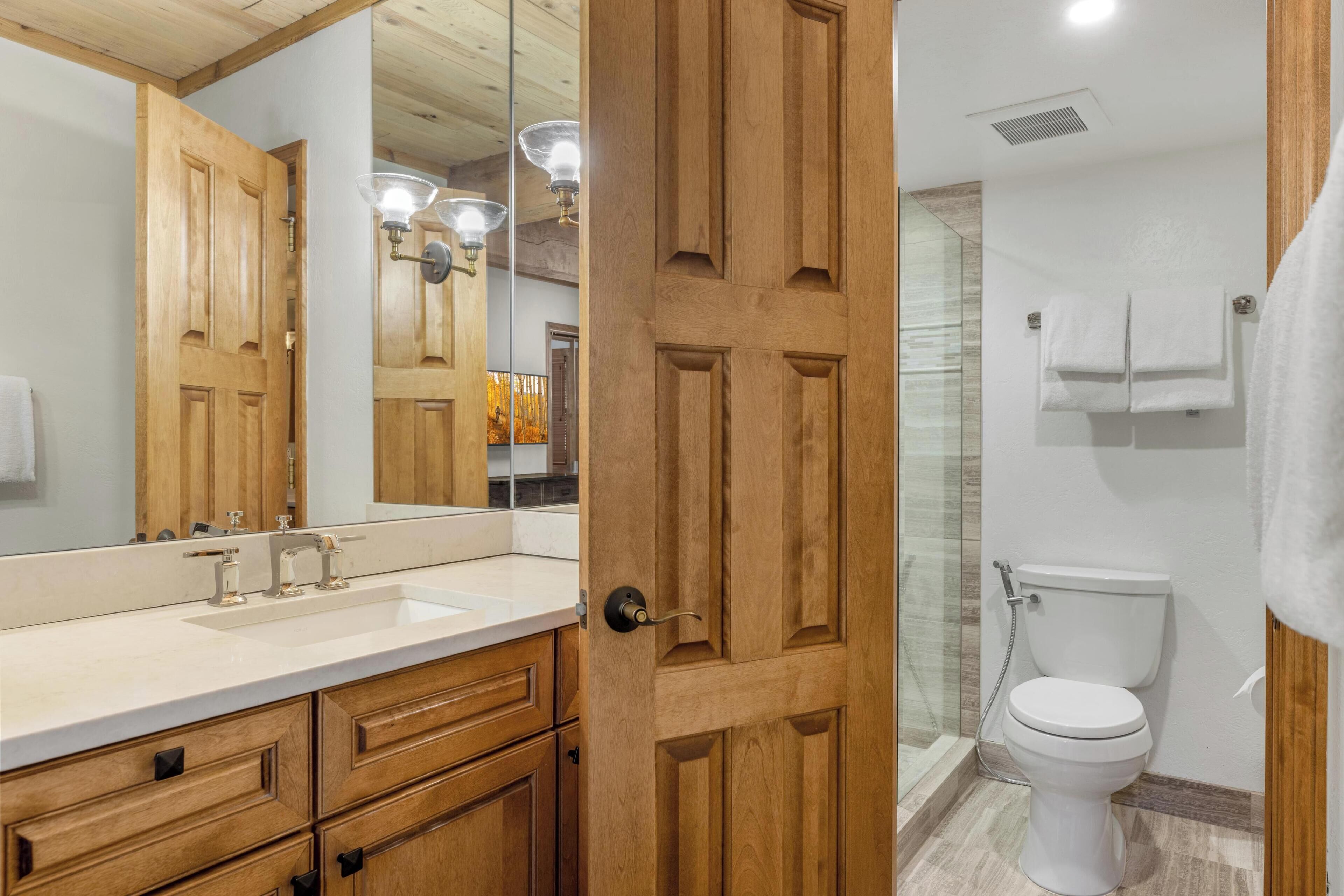 A bathroom with wooden cabinets, a sink, a toilet, and a shower.