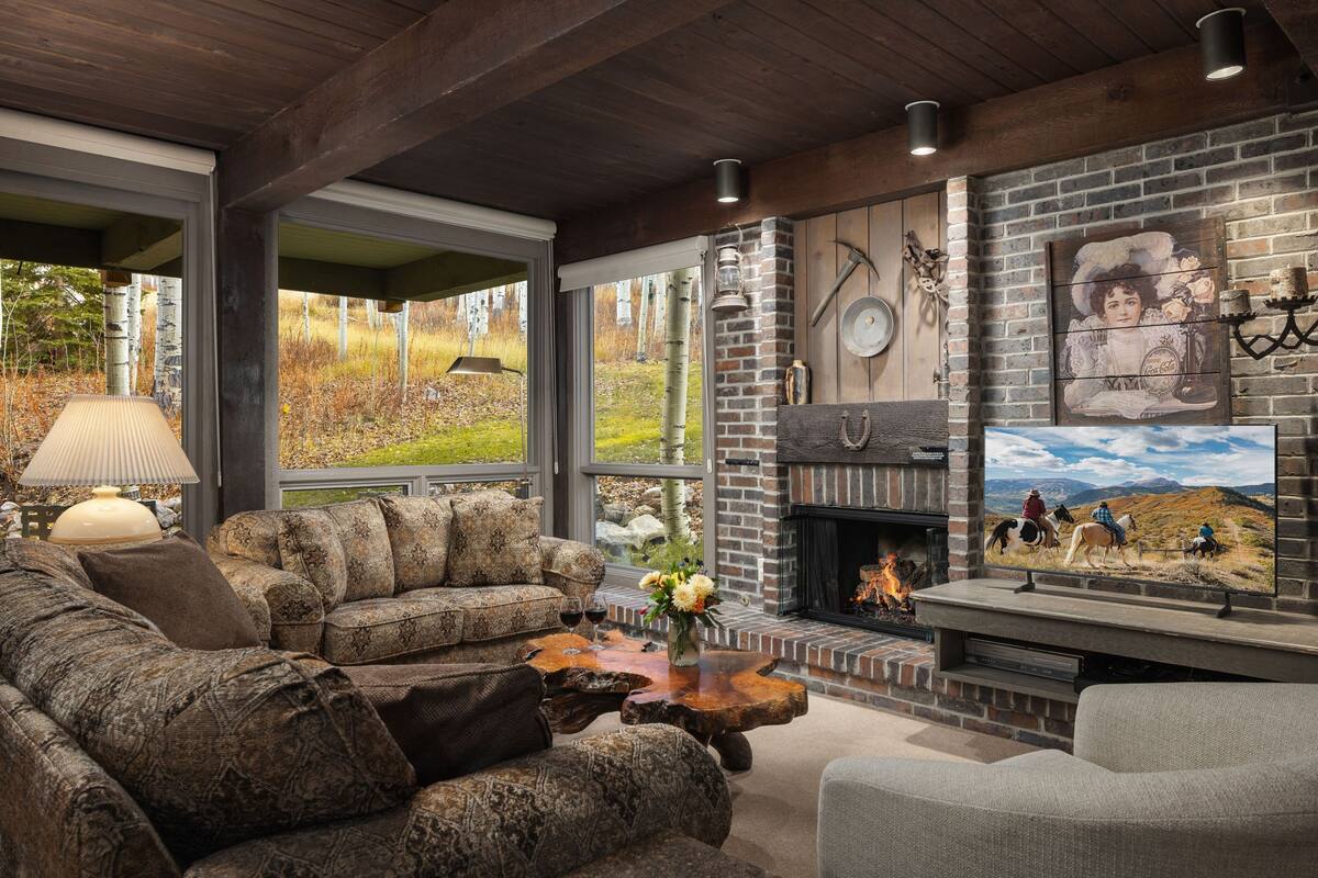 A cozy living room with a fireplace, a large window, and a rustic brick wall.
