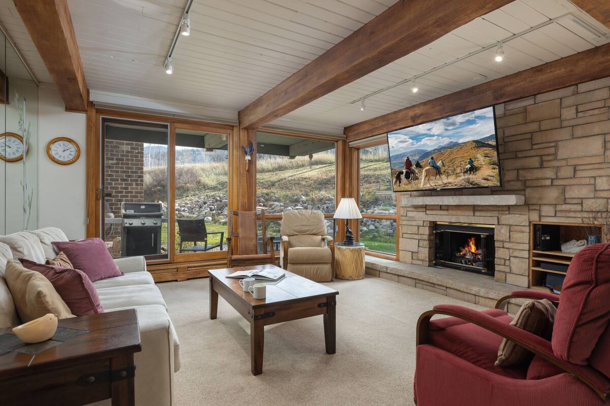 A living room with a stone fireplace, a sofa, a red armchair, and a television mounted on the wall.